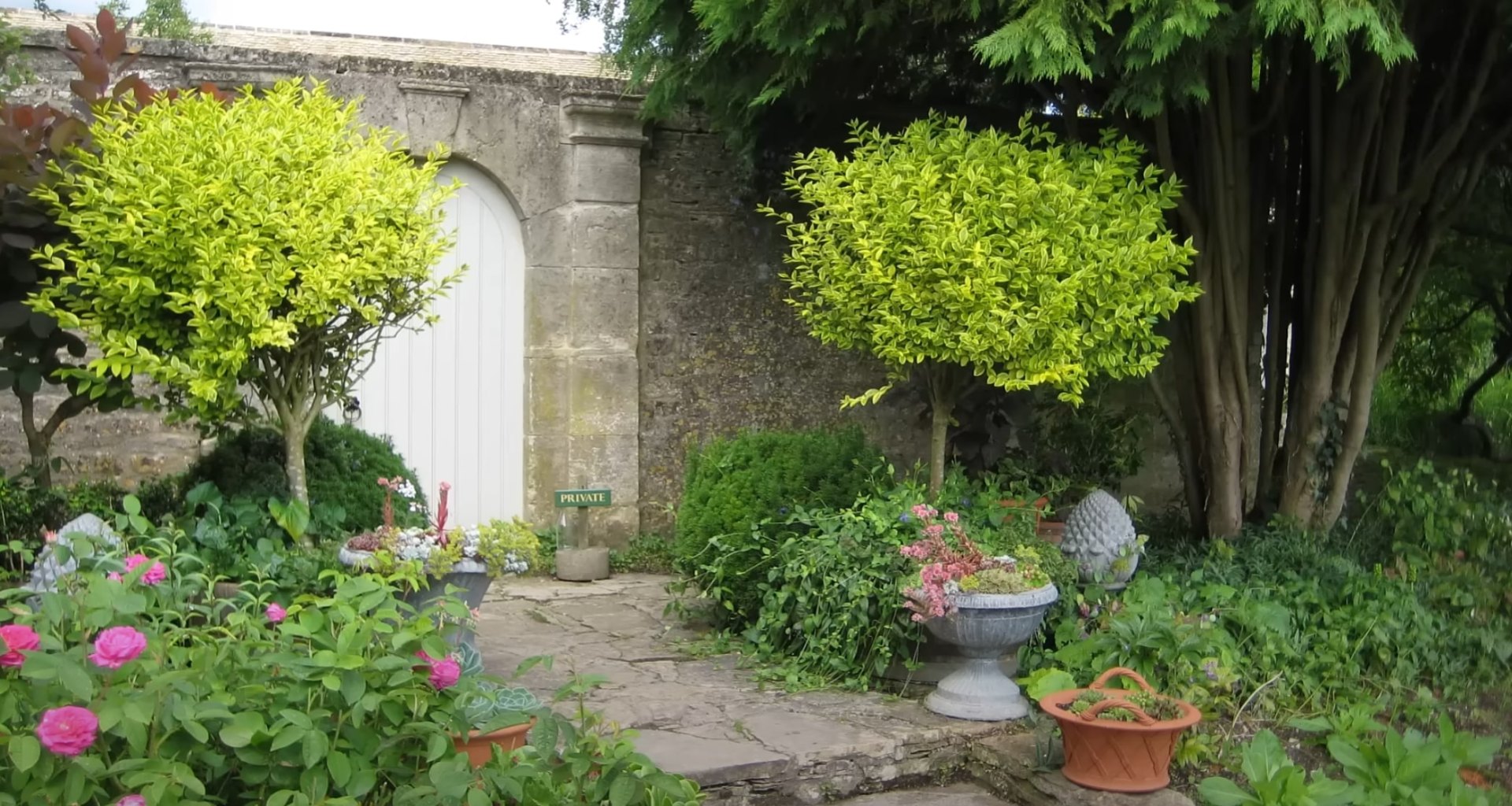 Maywood Landscaping Design - Custom Garden and Hardscape Installation Beautiful private garden with stone archway, flowering plants, and decorative containers showcasing professional landscape design